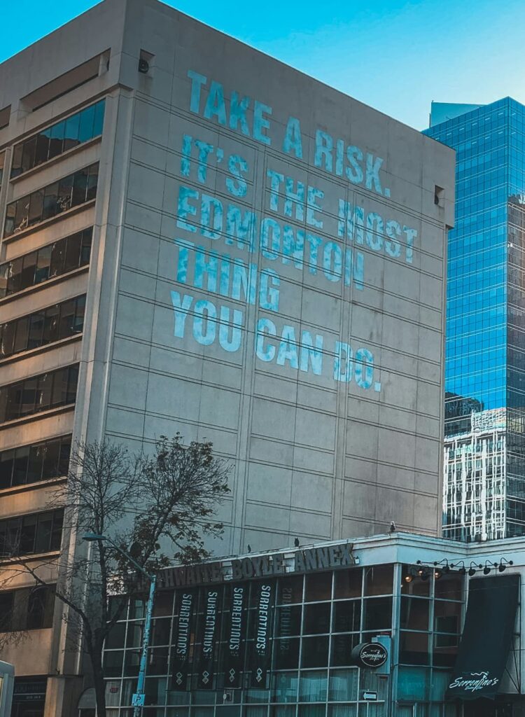 A mural on the side of a building that reads "Take a risk, it's the most Edmonton thing you can do."